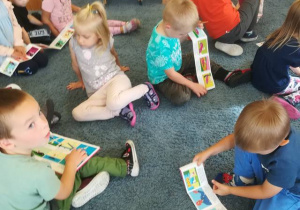 Dzieci siedzą na dywanie oglądają rozkładane książeczki ‘Przygody koziołka Matołka”